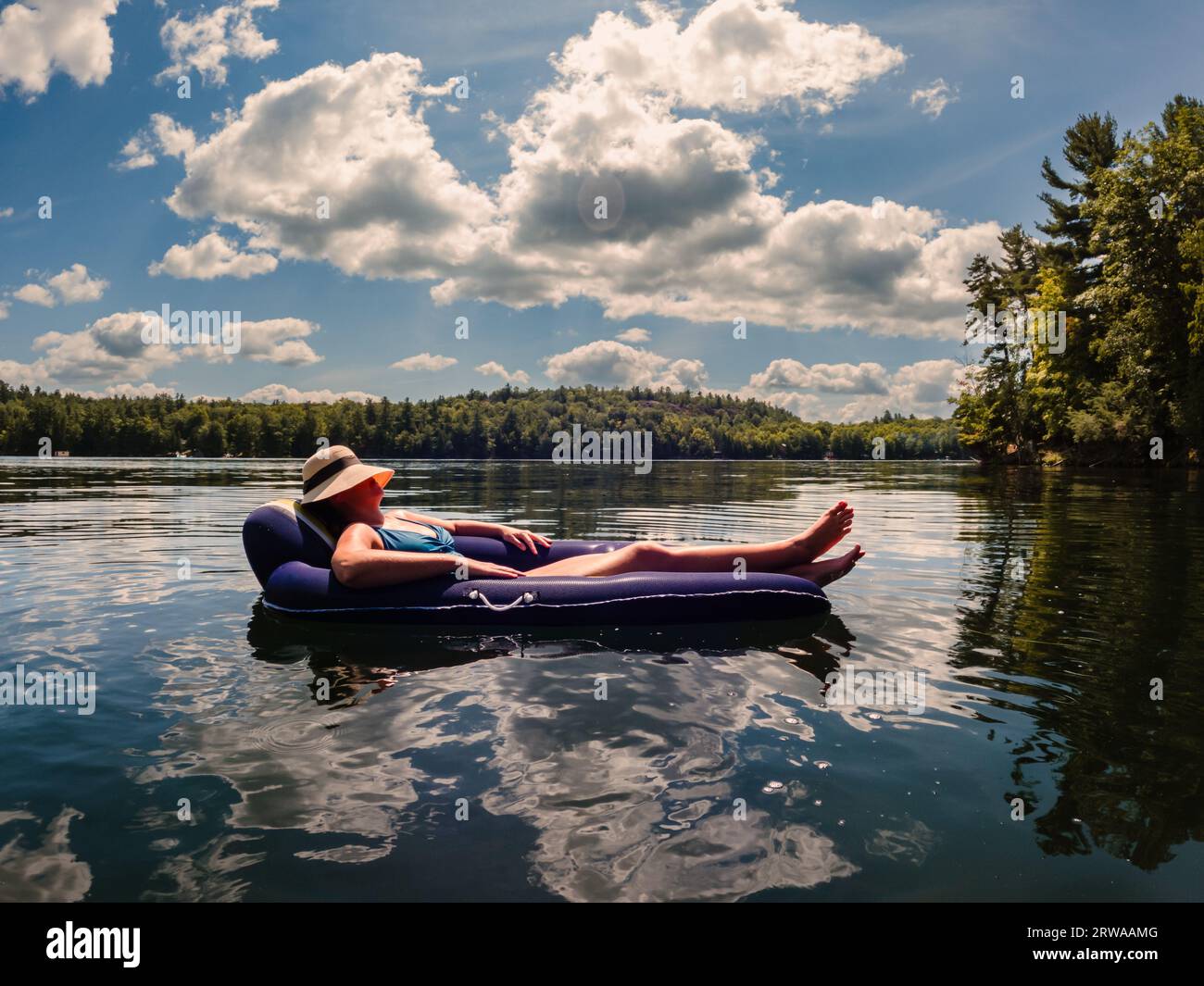 Woman in swimsuit floating on inflatable chair on lake in summer. Stock Photo