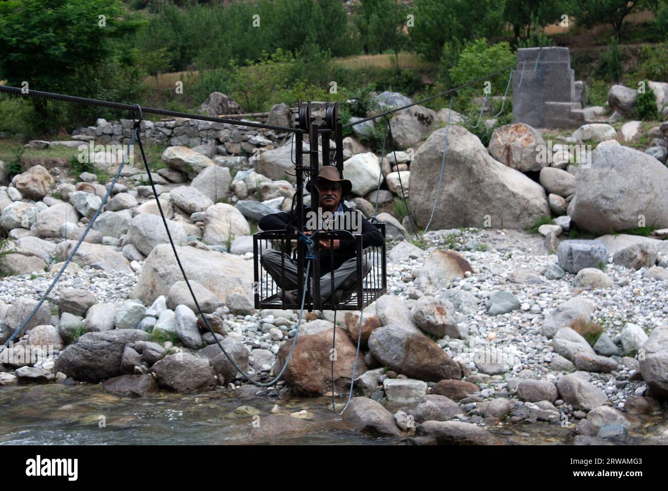 Man Crossing a river in a hand pulled pulley, Himalayas, Himachal Pradesh, India Stock Photo