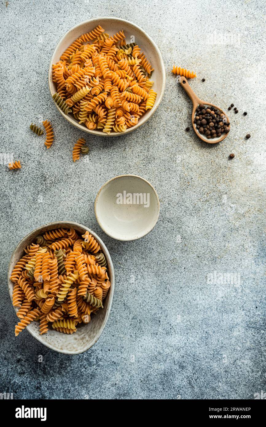 Overhead view of two bowls of uncooked fusilli pasta and a bowl of black peppercorns on a table Stock Photo