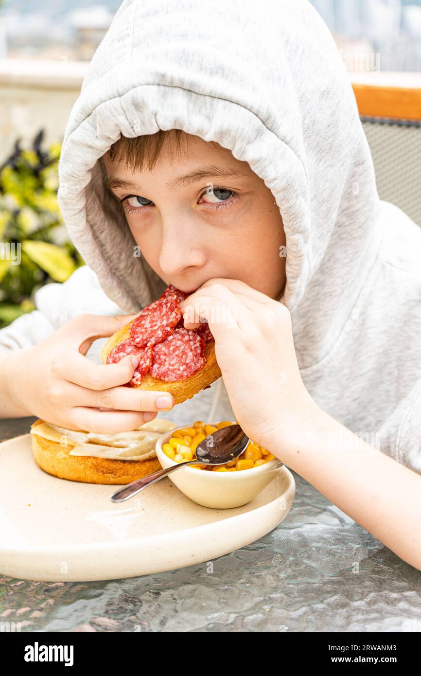 Boy has a snack with toastes with cheese and pepperoni sausages outdoor Stock Photo