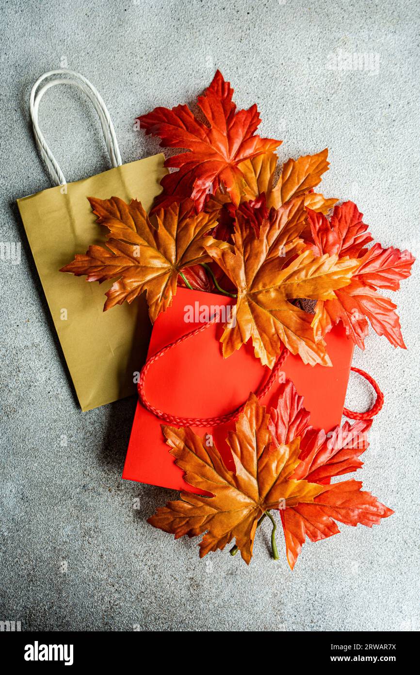 Autumnal sale concept with paper bags and bright leaves on concrete background Stock Photo