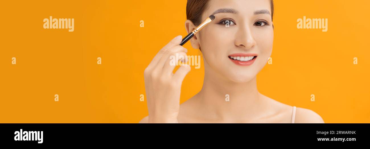 Yellow banner studio photo of a young woman using make up brush and eye shadows. Stock Photo