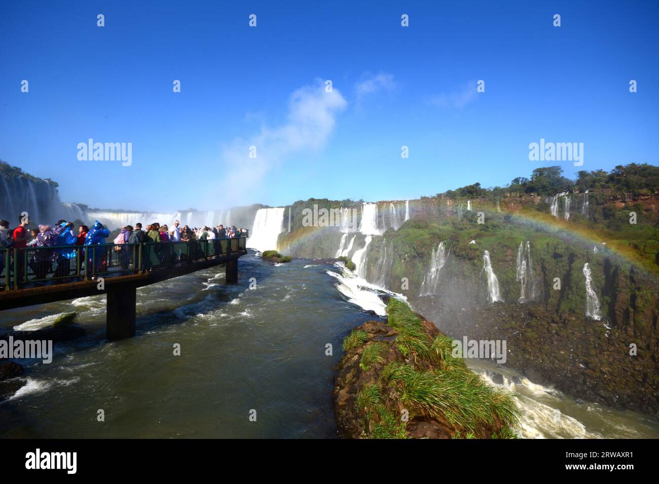 Tourists at Iguazu Falls, one of the great natural wonders of the world, on the border of Brazil and Argentina with a rainbow on the right. Stock Photo