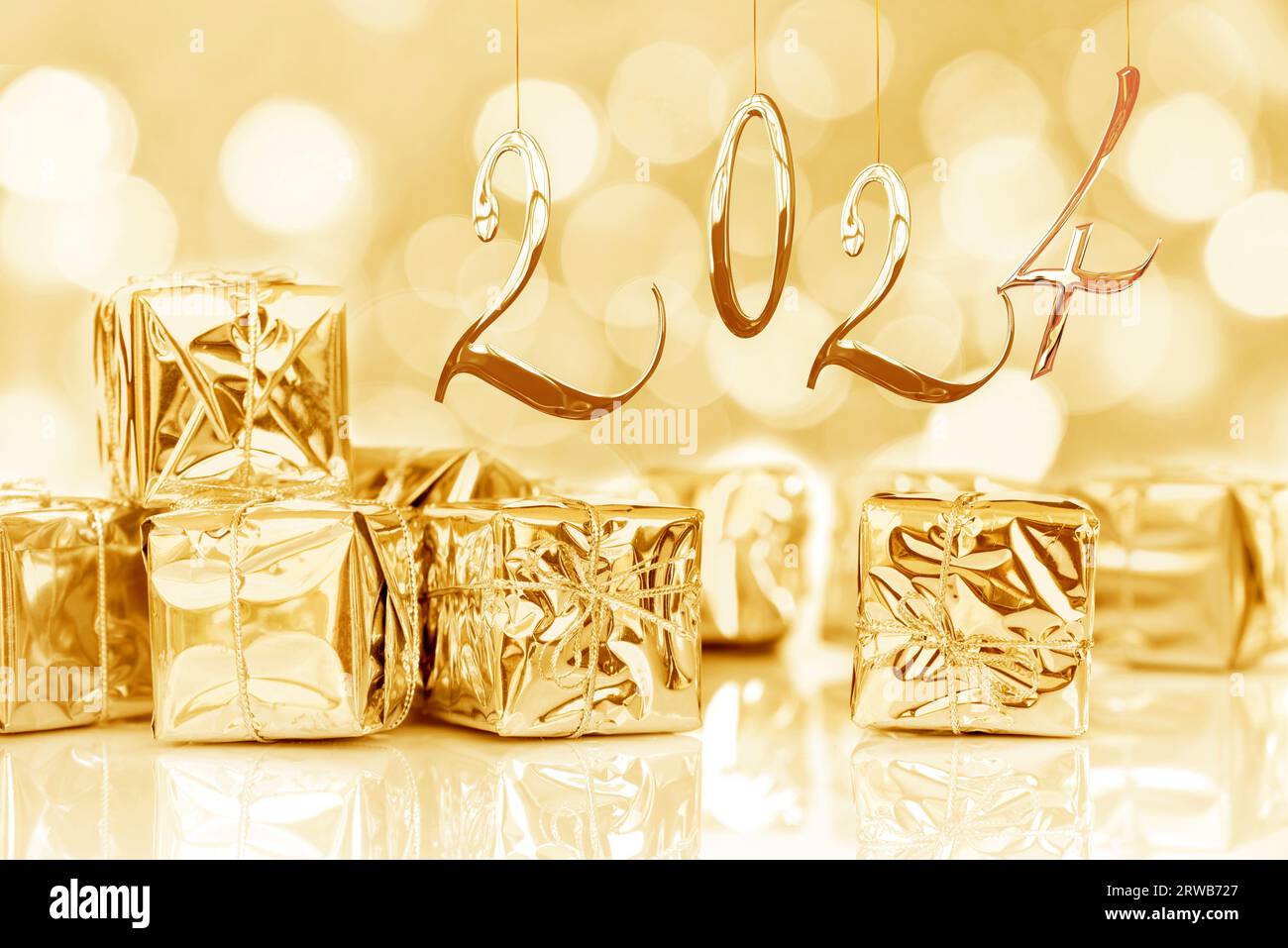 2024, new year card. Small Christmas gifts in shiny golden paper, bokeh lights background Stock Photo