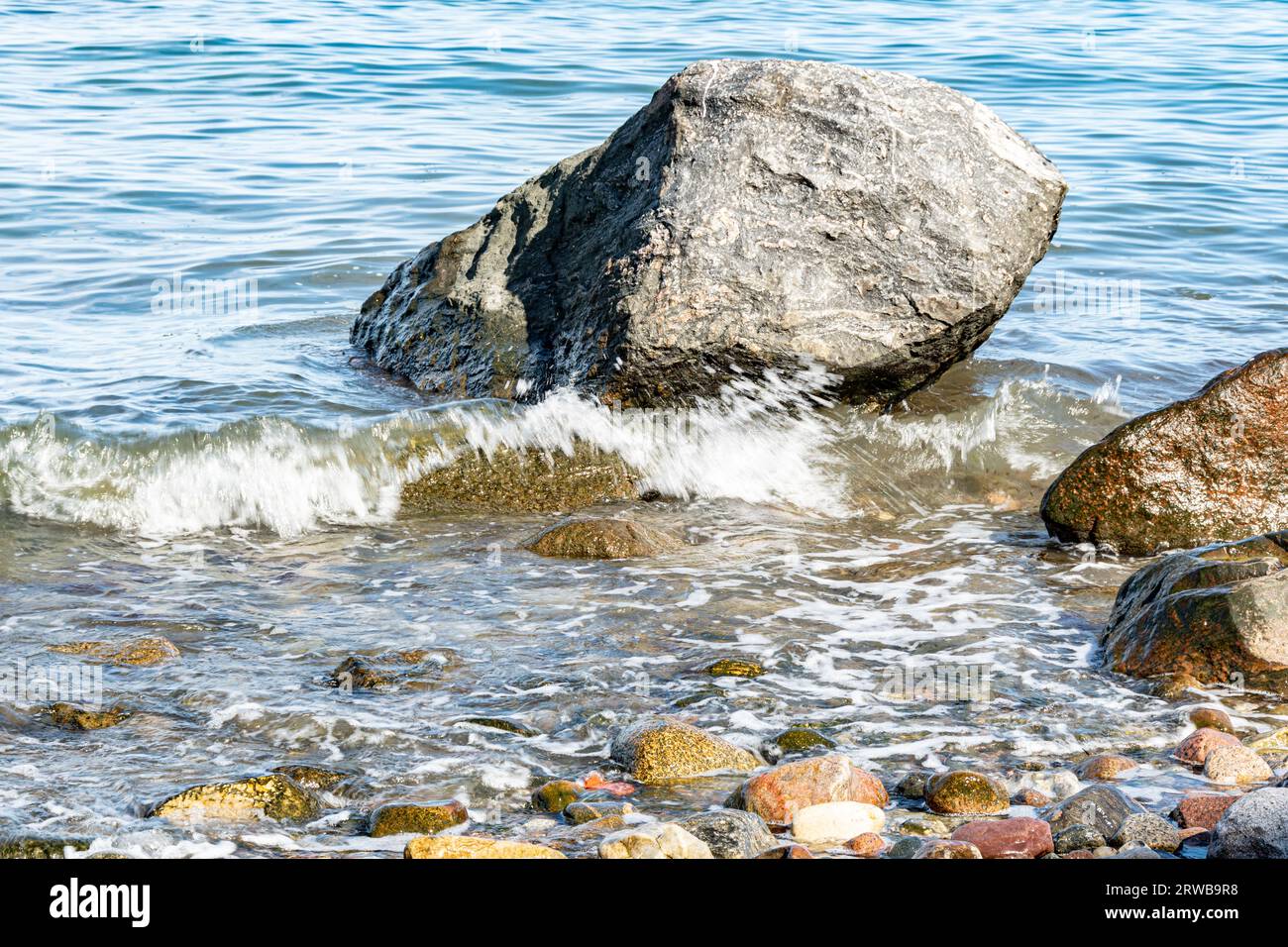 Stein In der Ostsee. Eine kleine Welle überspült den kleinen Nachbarn Stock Photo