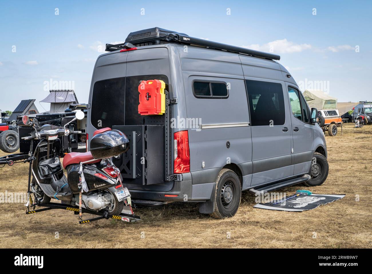 Loveland, CO, USA - August 26, 2023: 4x4 camper van on Mercedes Sprinter chassis with Vespa scooter on a hitch rack in a busy campground. Stock Photo