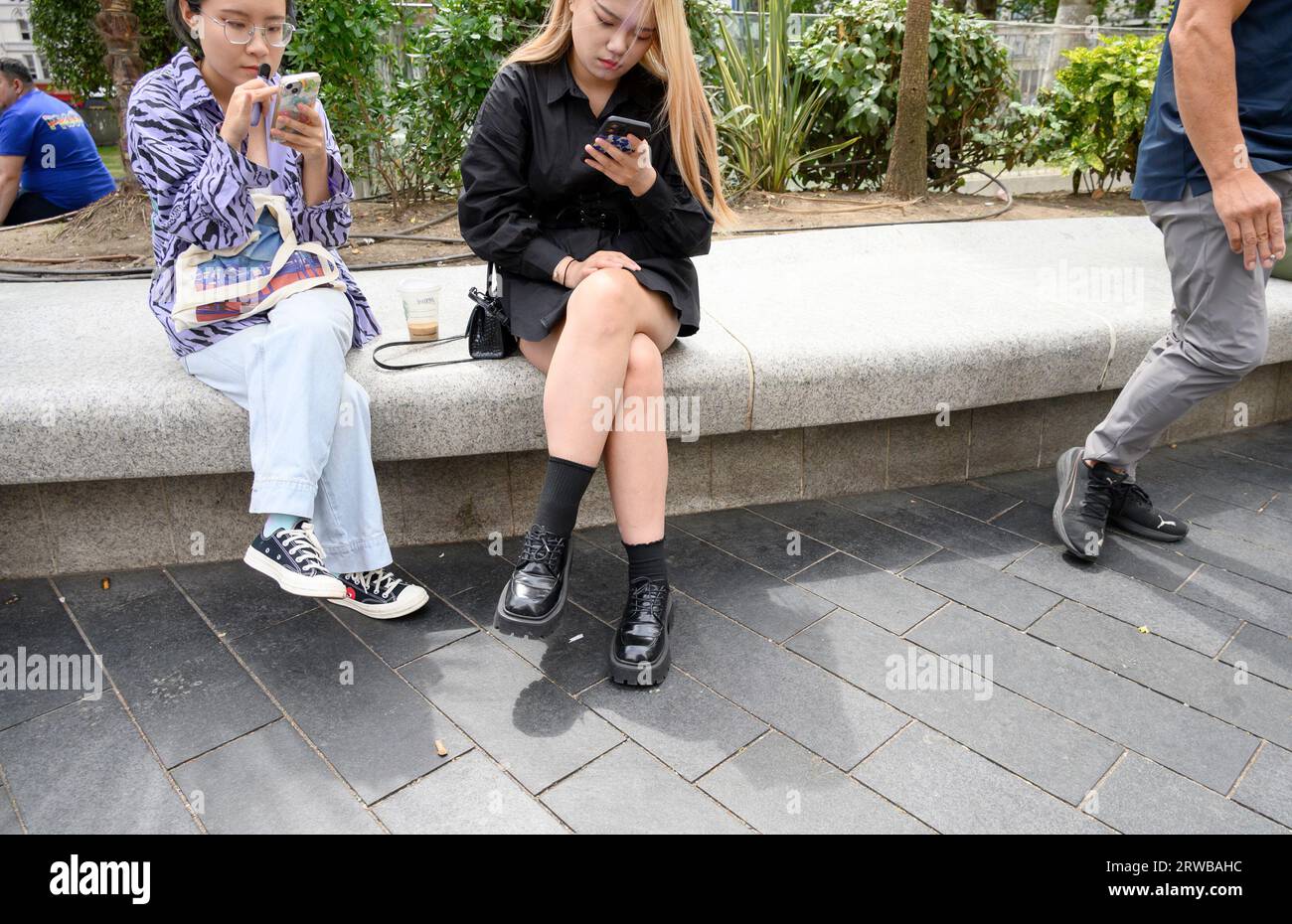 London, England, UK. Two young Asian women looking at their mobile phones in Leicester Square Stock Photo
