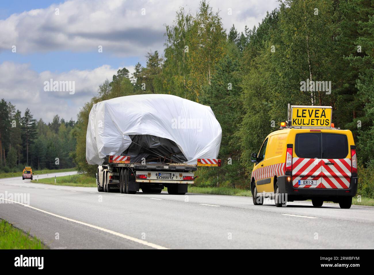 Truck transports oversize load on flatbed trailer towards Hanko port. The transport has pilot vehicles front and back. Raasepori, Finland. Sept 8, 23 Stock Photo