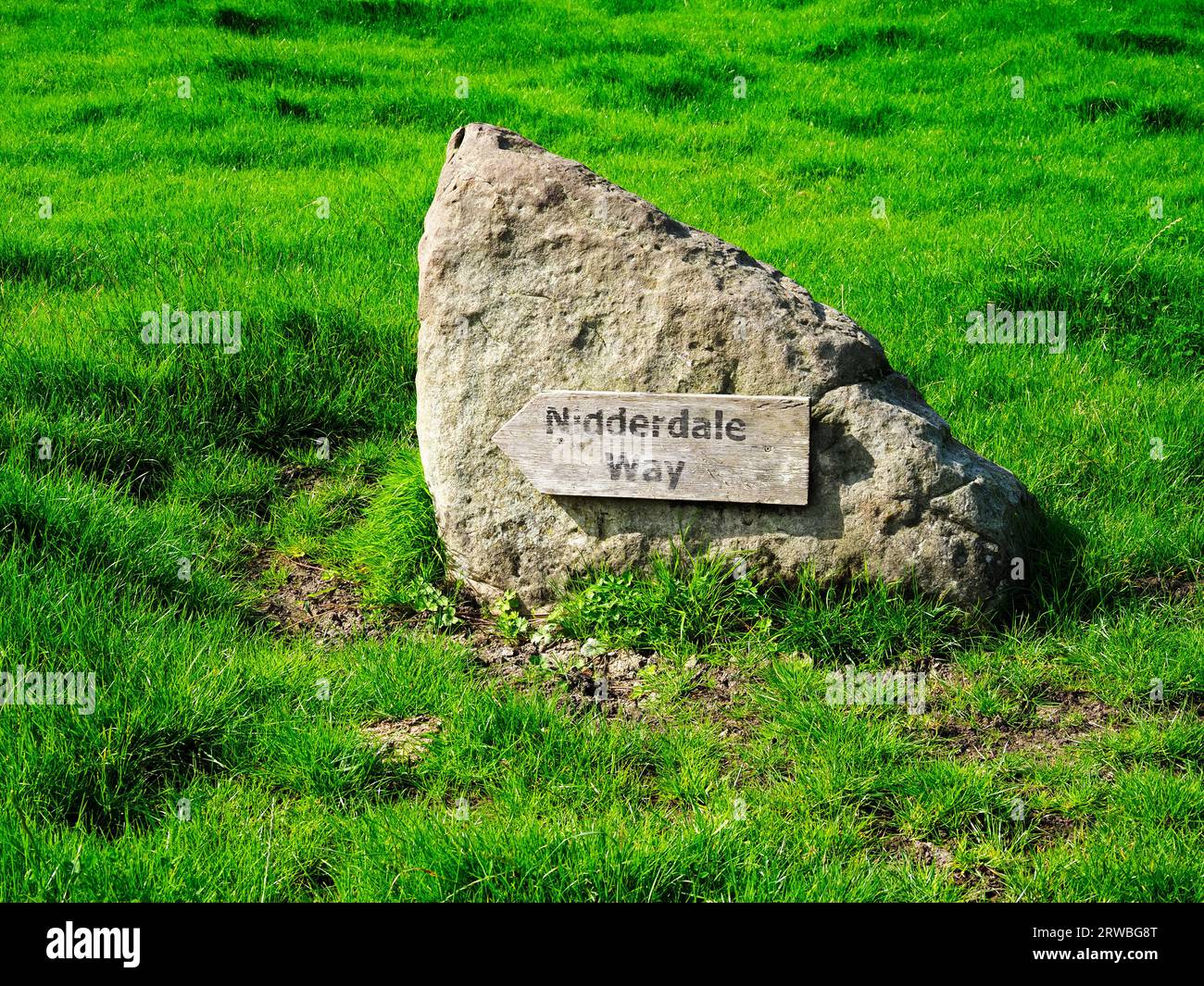 A Nidderdale Way sign on a boulder in a farmyard near Dacre Banks Nidderdale North Yorkshire England Stock Photo