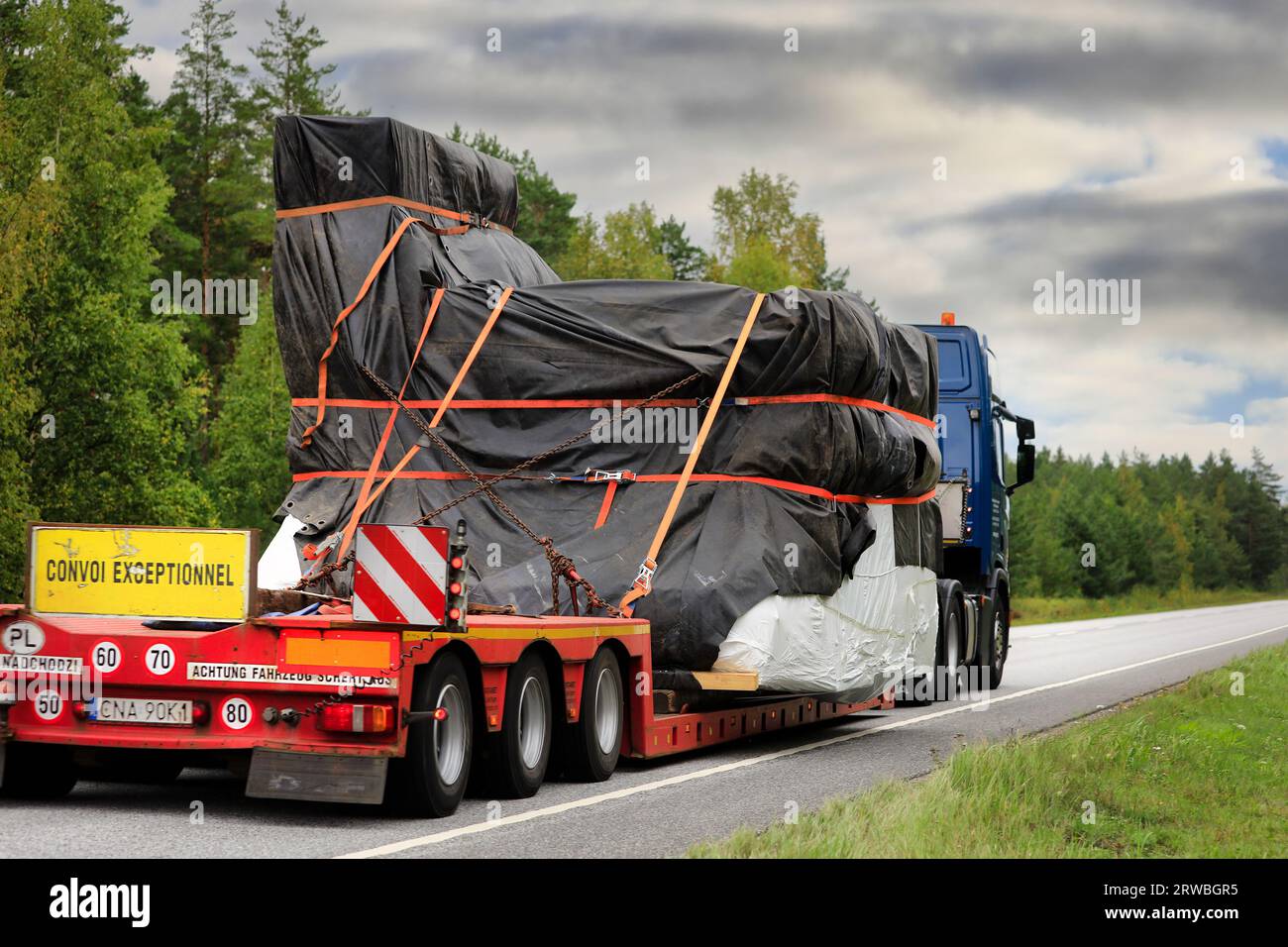 Scania truck low loader trailer hauls tarpaulin covered object as oversize load on road, rear view, focus on load. Raasepori, Finland. Sept 8, 2023. Stock Photo