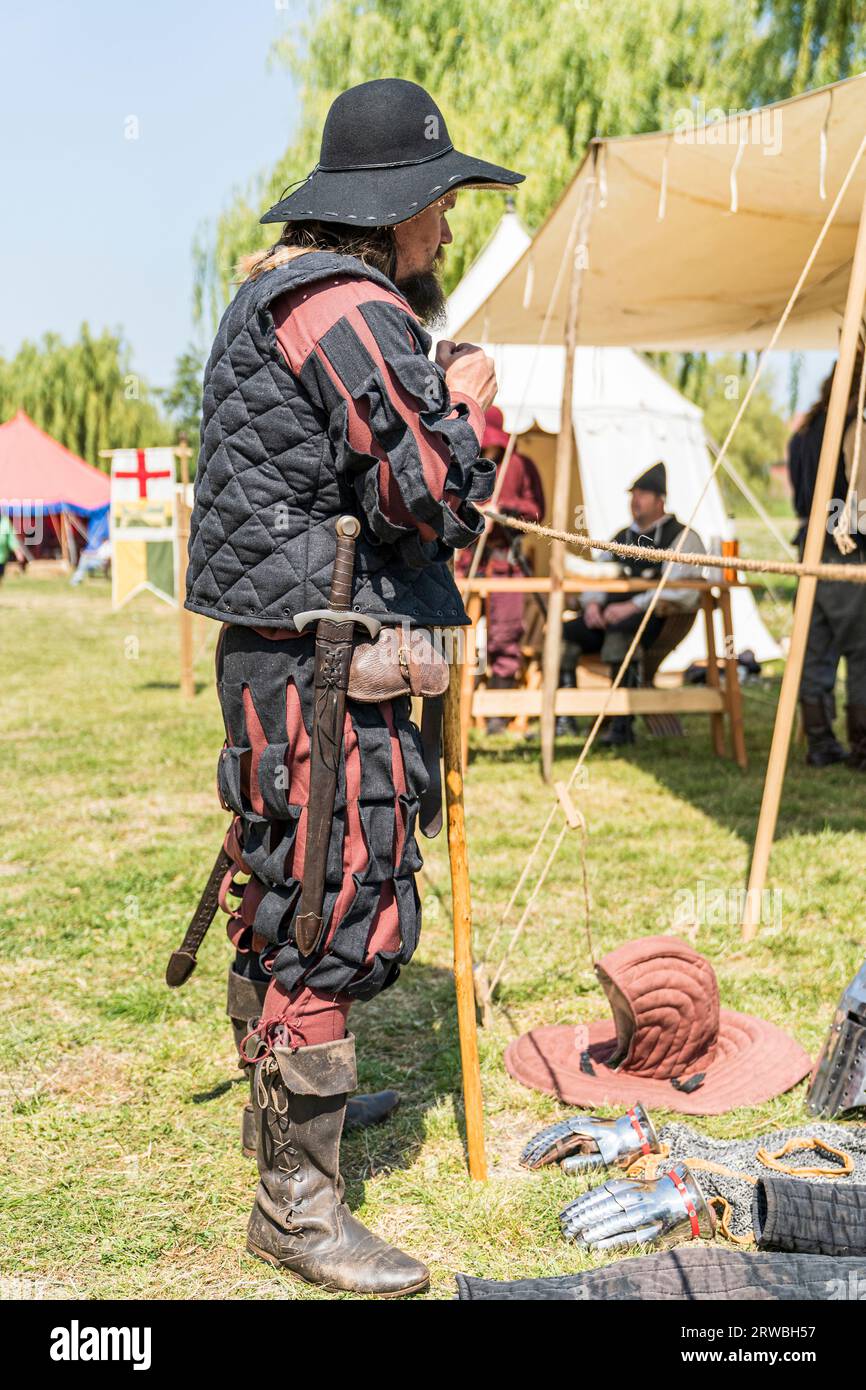 Man dressed up as a mercenary of the Middle ages during a medieval living history event. Side view of the man standing wearing a black and red uniform Stock Photo