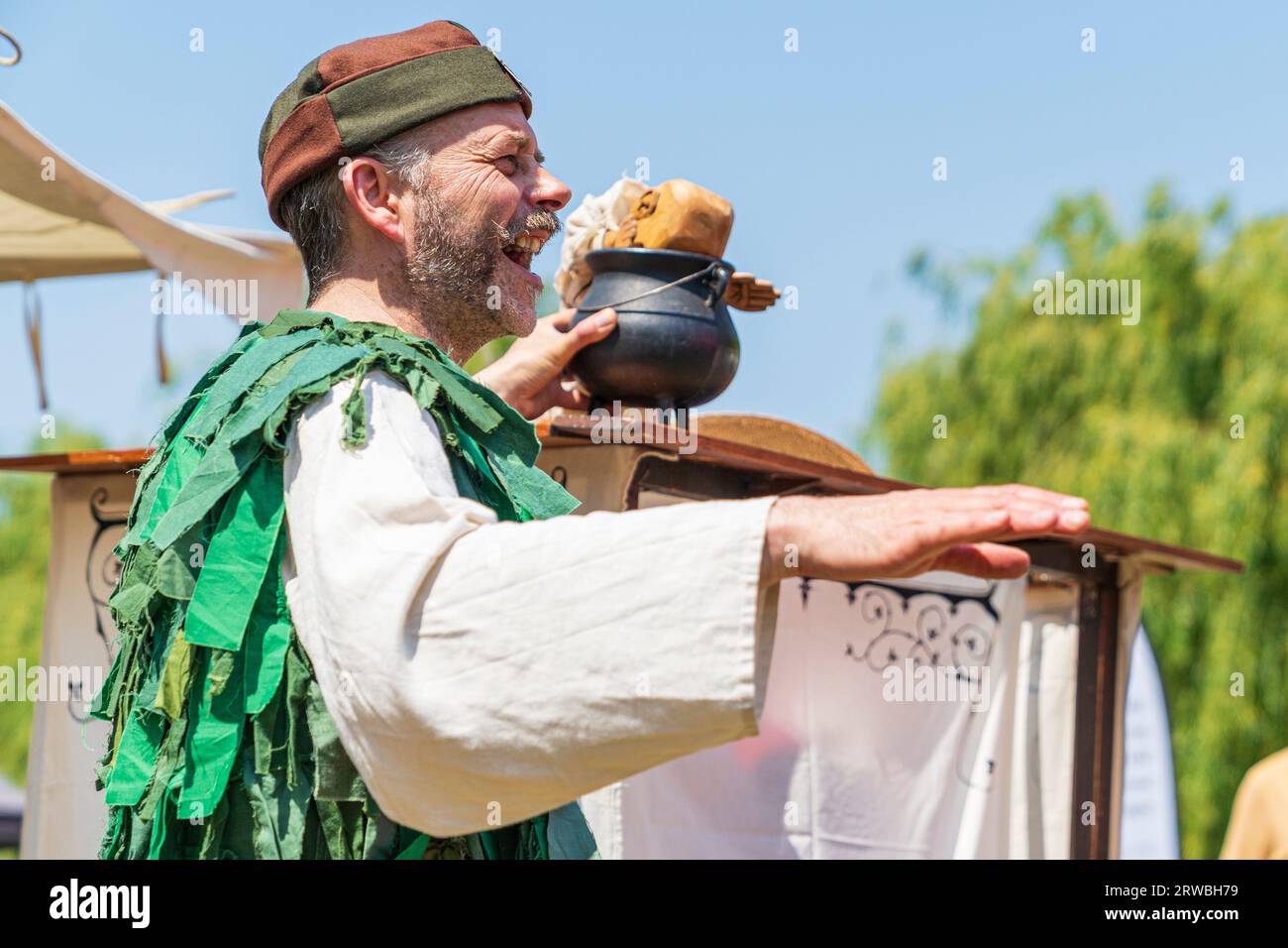 Medieval puppeteer in a green period costume, performing with puppet during a reenactment event at Sandwich town in kent in the summertime. Stock Photo