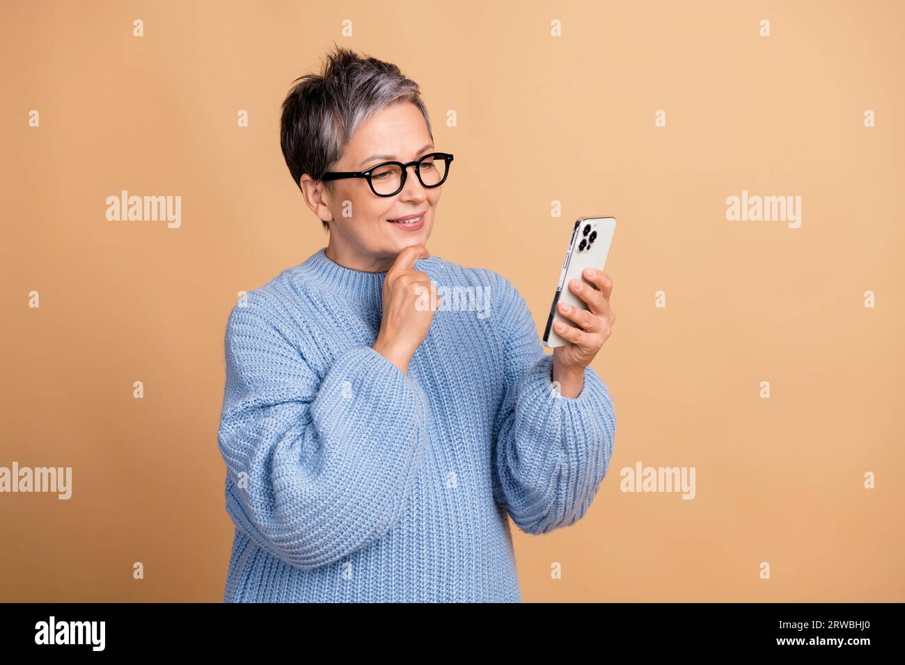 Portrait of minded creative lady hand touch chin use samrt phone empty space isolated on beige color background Stock Photo