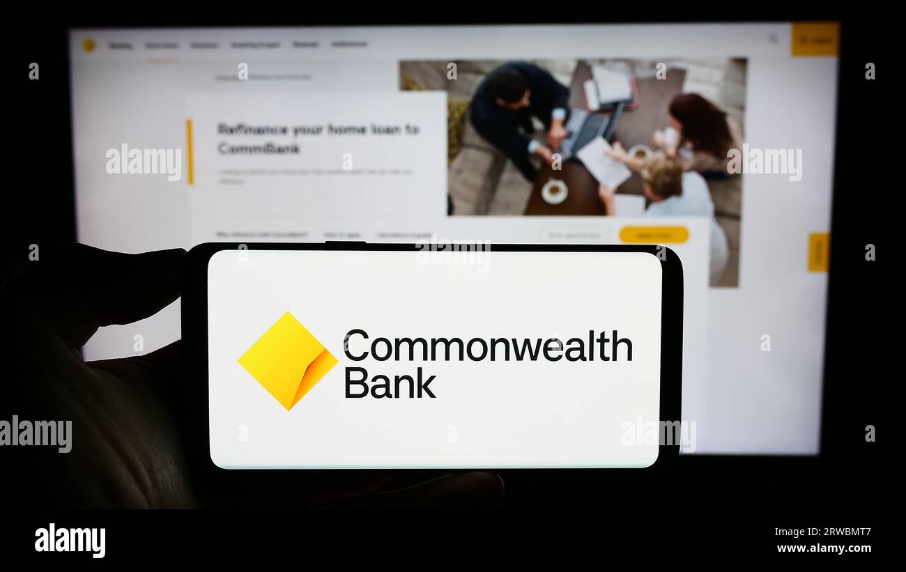 Person holding smartphone with logo of company Commonwealth Bank of Australia (CBA) on screen in front of website. Focus on phone display. Stock Photo