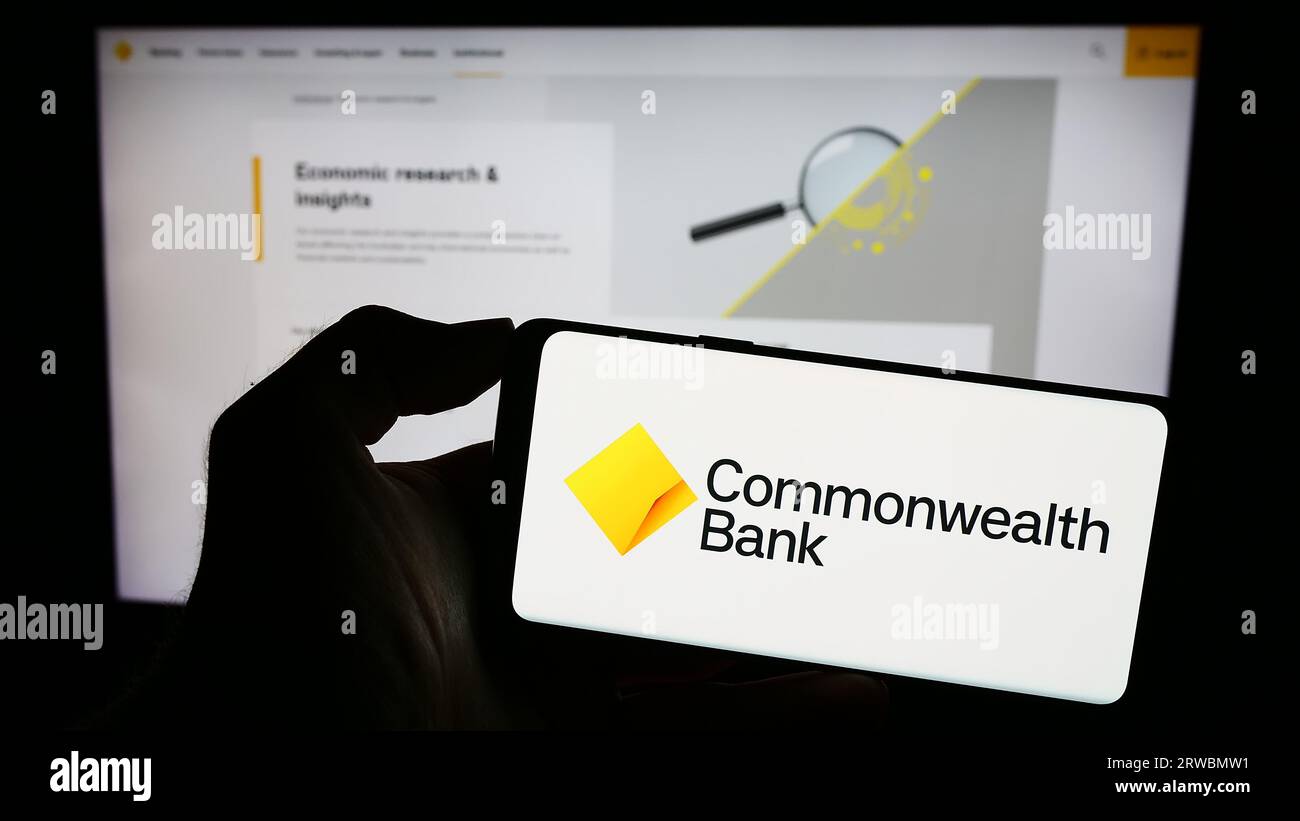 Person holding cellphone with logo of company Commonwealth Bank of Australia (CBA) on screen in front of webpage. Focus on phone display. Stock Photo