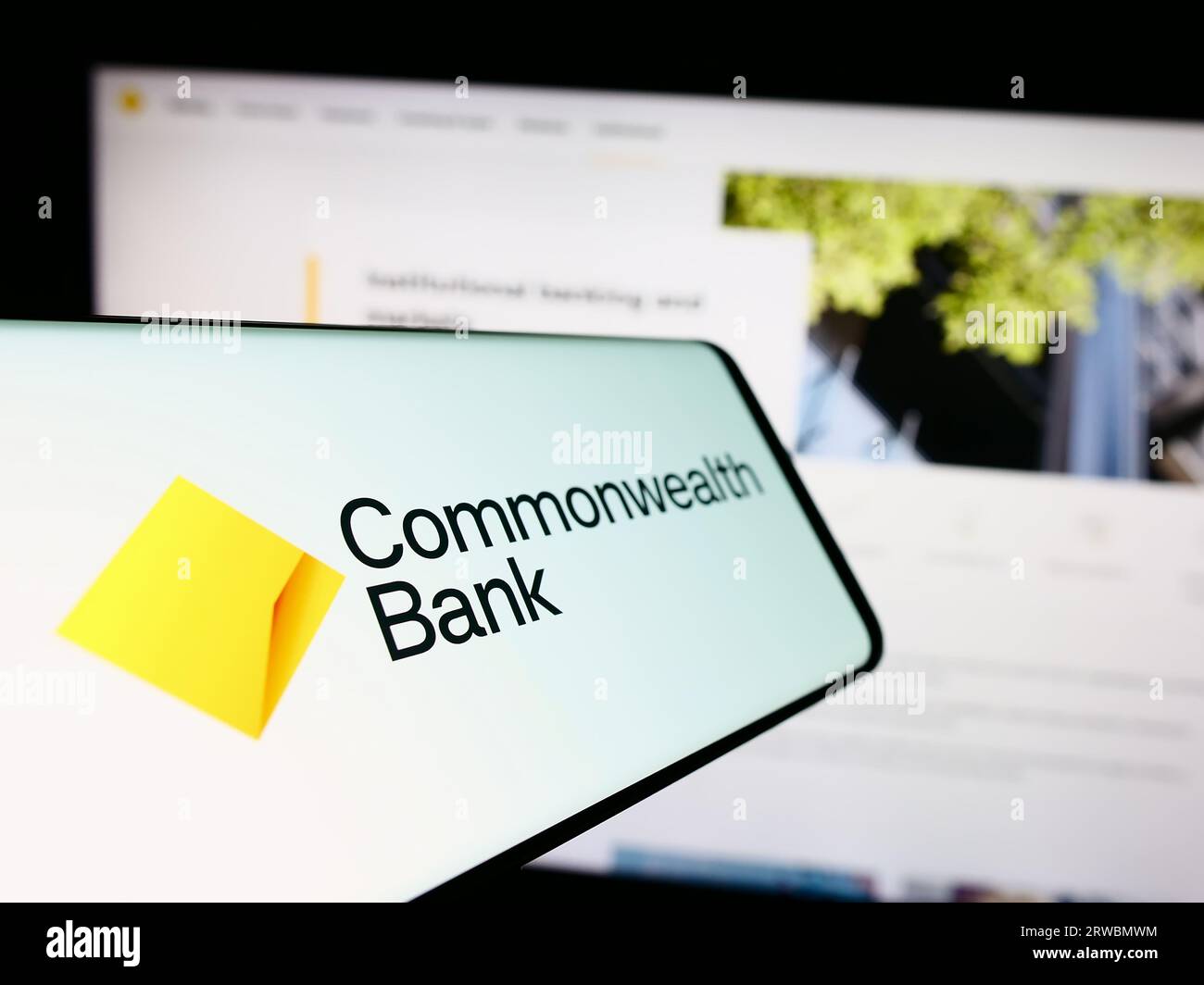 Smartphone with logo of company Commonwealth Bank of Australia (CBA) on screen in front of website. Focus on center-left of phone display. Stock Photo