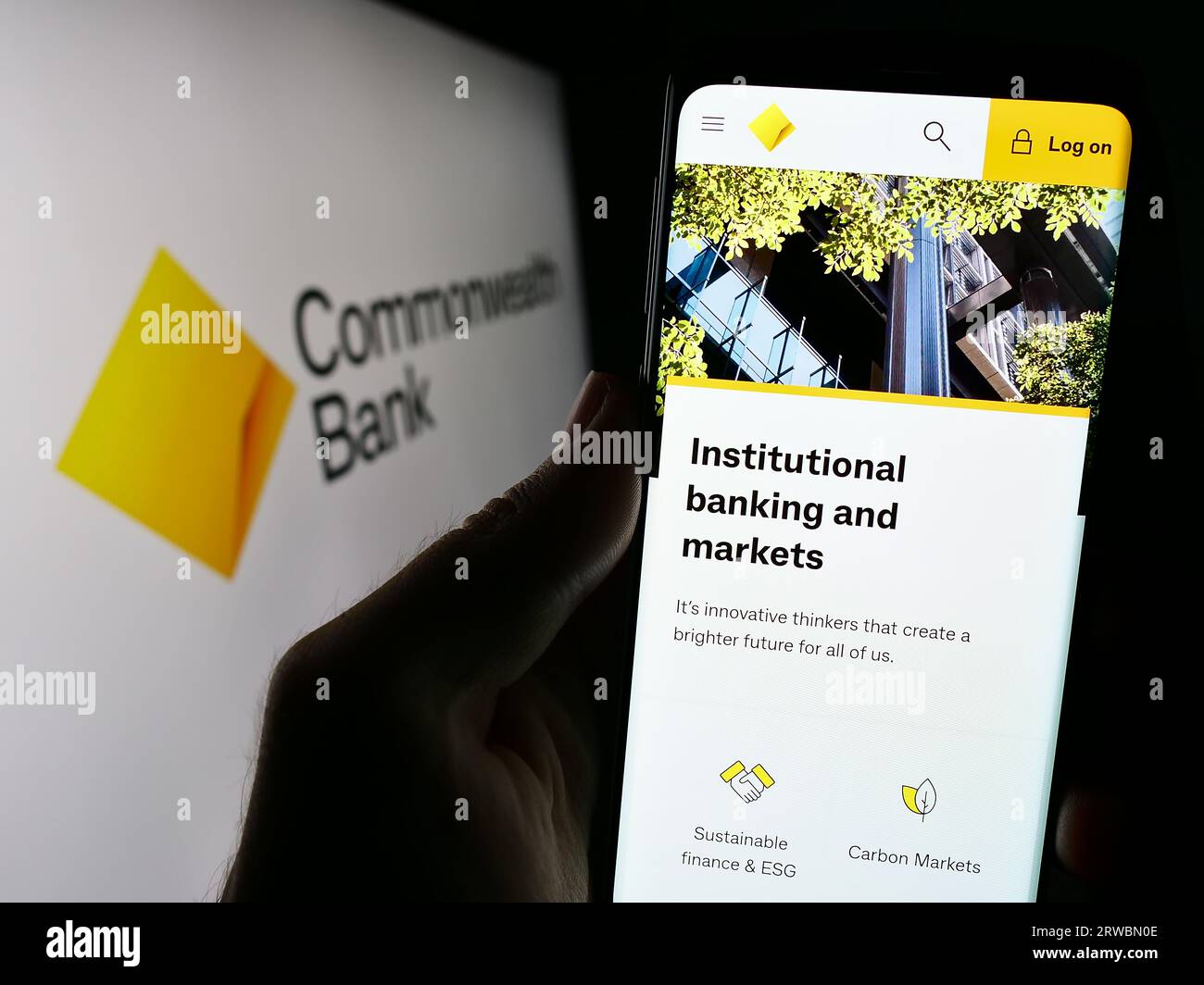 Person holding cellphone with webpage of company Commonwealth Bank of Australia (CBA) on screen with logo. Focus on center of phone display. Stock Photo
