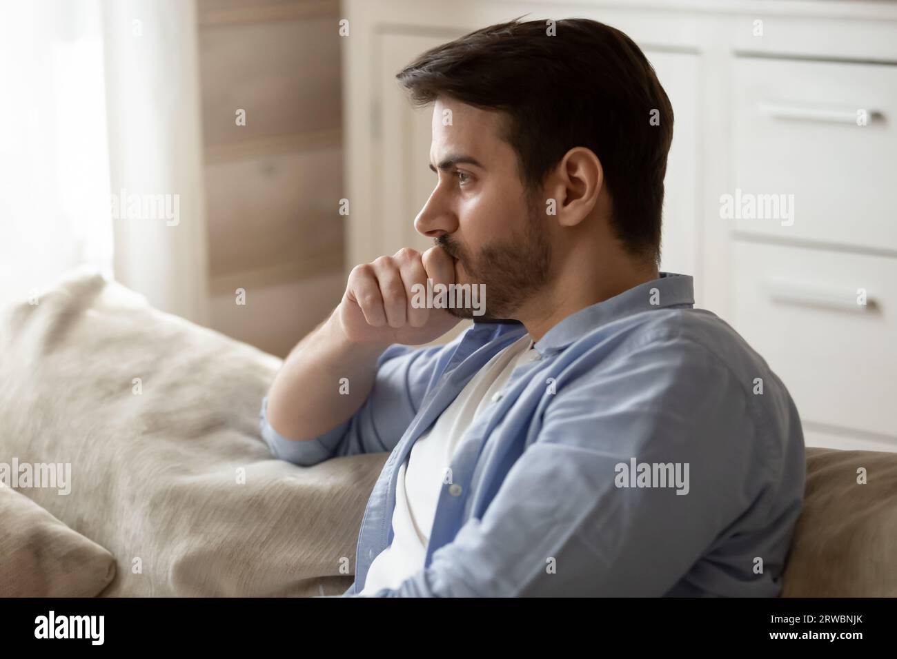 Thoughtful upset man pondering problem solving, sitting on couch Stock Photo