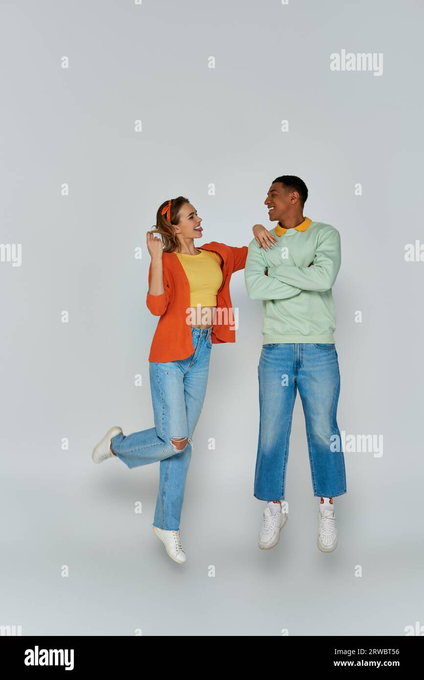 happy young woman sticking out tongue and looking at african american man on grey backdrop, levitate Stock Photo