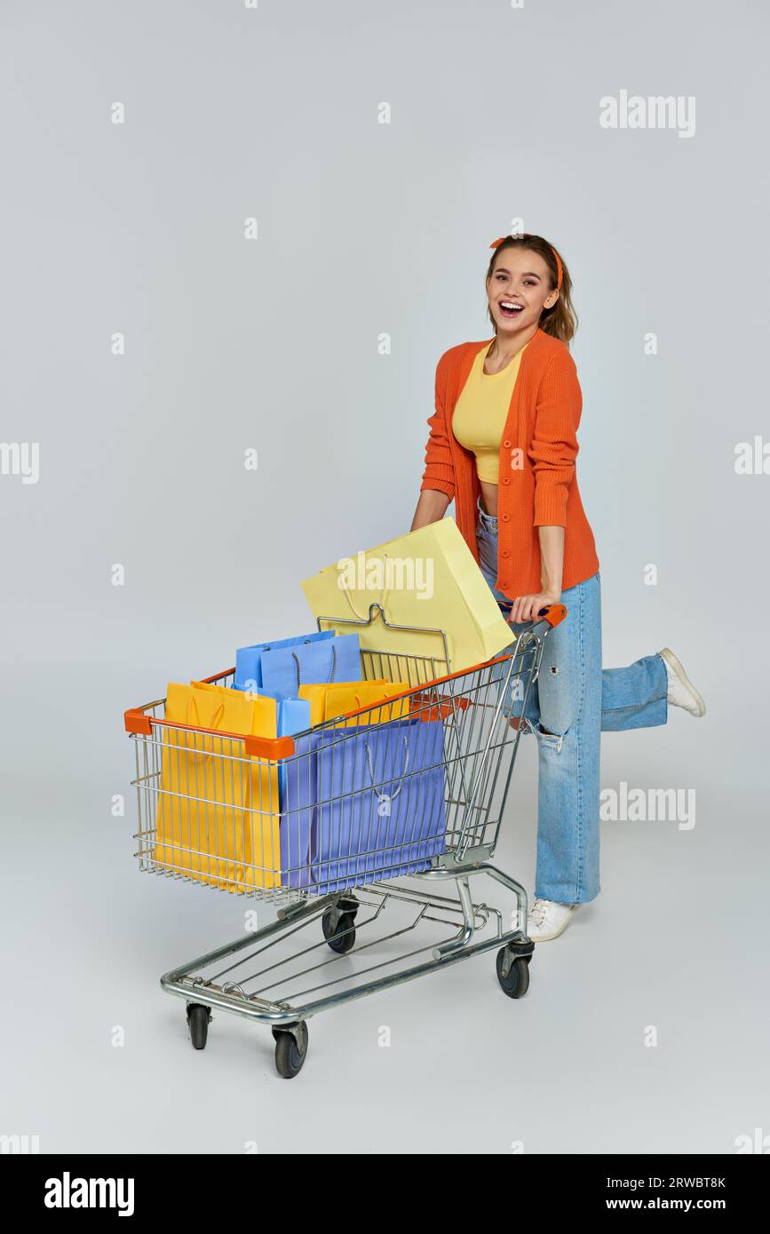 excited woman riding trolley with colorful shopping bags on grey backdrop,  consumerism and sales Stock Photo - Alamy, image size:867x1390