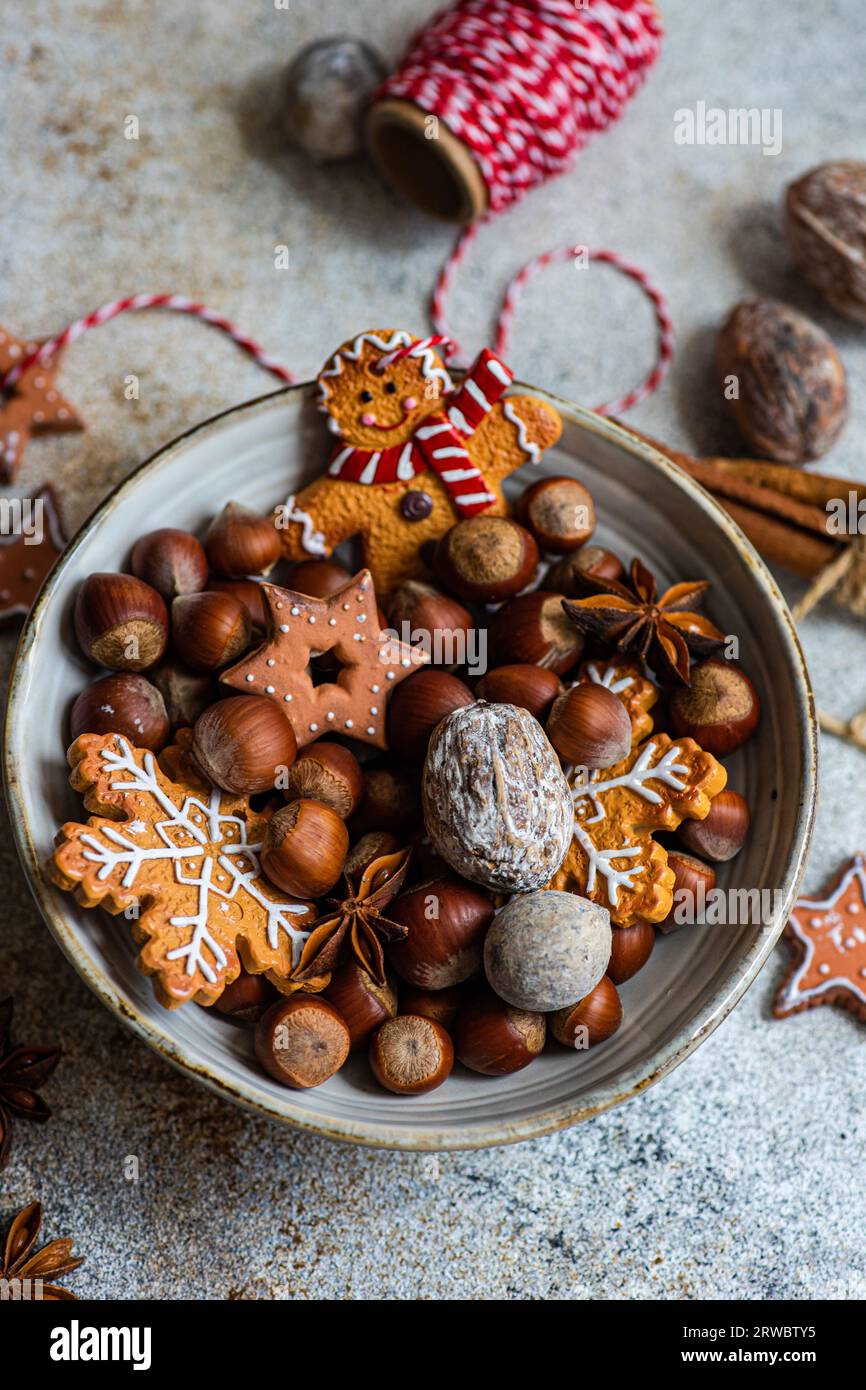Top view of plate of heap of chestnuts with tasty Christmas cookies placed on table near spool of red thread Stock Photo