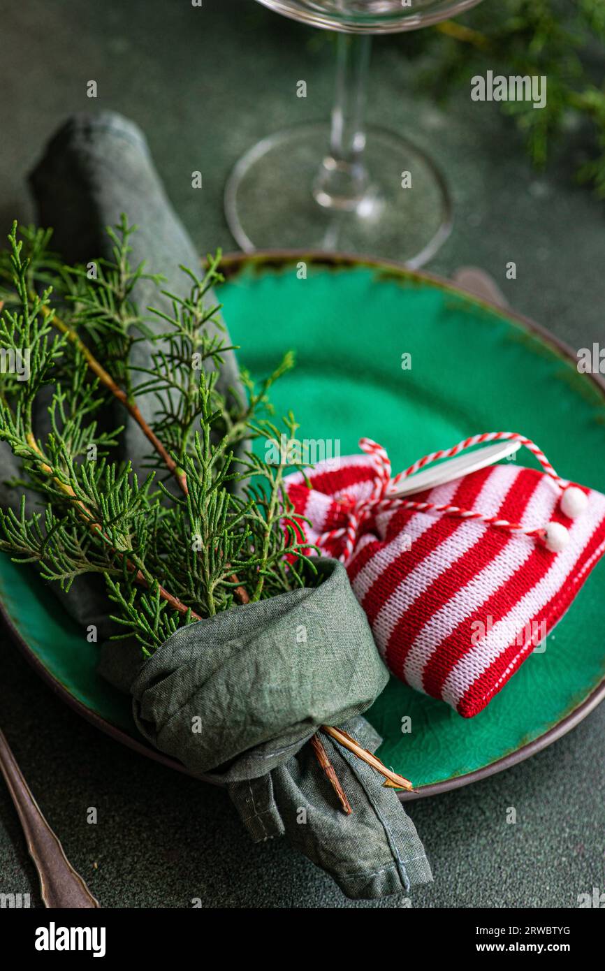 Little Christmas bag and fir sprigs wrapped in handkerchief on plate placed on green table near glass and forks Stock Photo