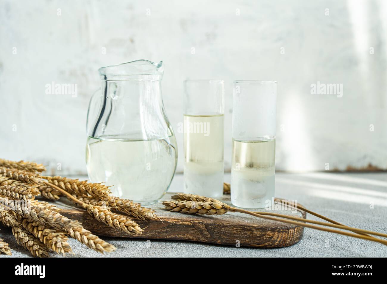 Traditional Ukrainian alcoholic drink made from wheat and known as Gorilka served in transparent jar and glasses placed on cutting board against blurr Stock Photo