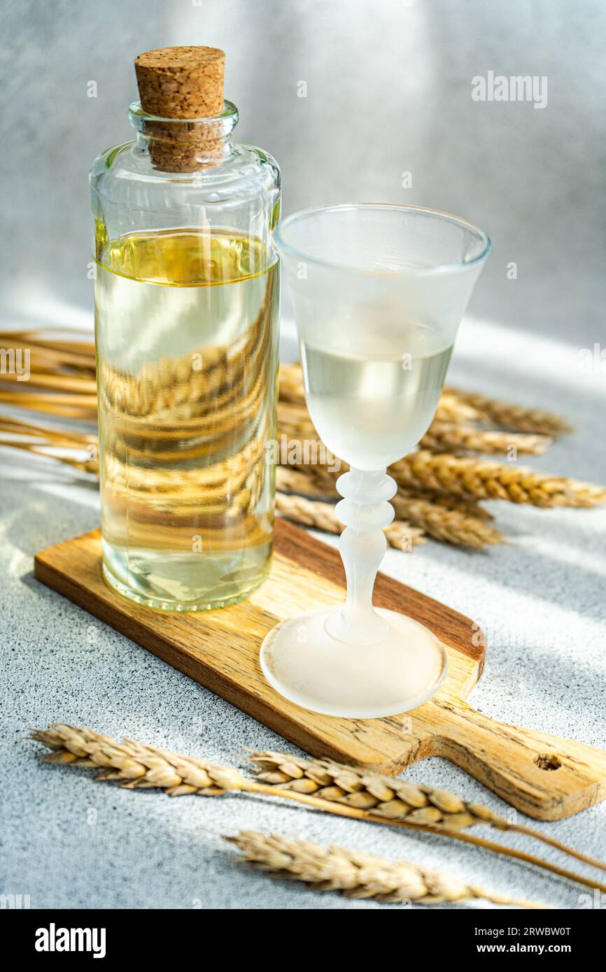 Traditional Ukrainian alcoholic drink made from wheat and known as Gorilka served in transparent glass near bottle placed on cutting board against blu Stock Photo