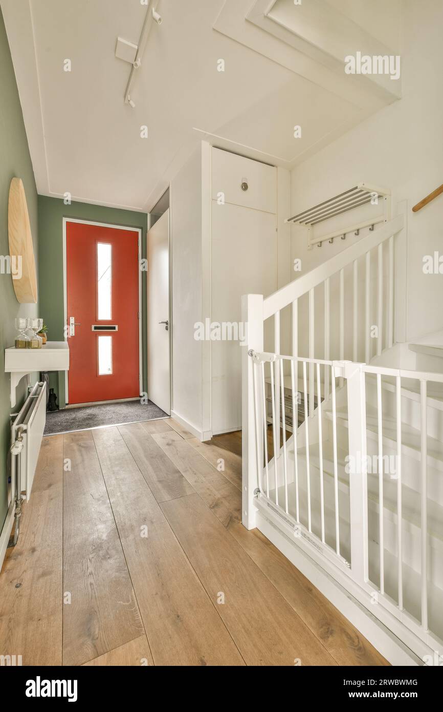 Interior of modern house with red closed door and white staircase to upper floor with railing in hallway Stock Photo