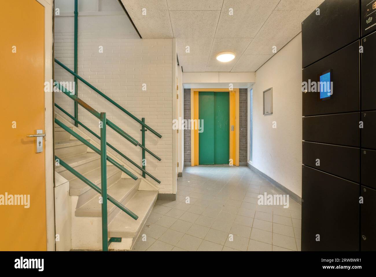 Interior of modern office building with empty hallway leading to green elevator and white tiles on floor Stock Photo