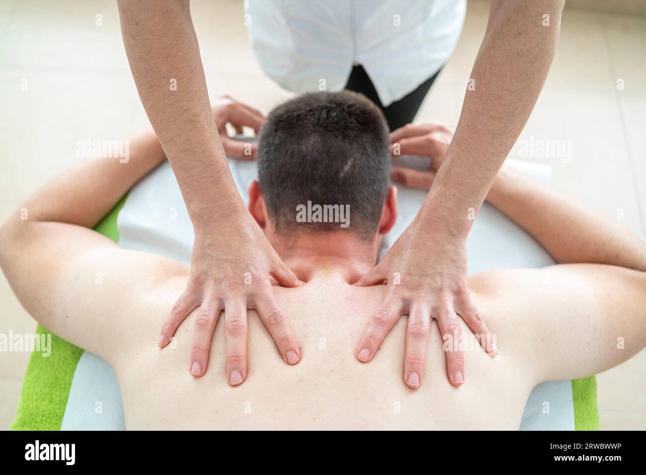 High angle of unrecognizable professional therapist pressing the back of a male patient lying on a table during a massage session at a clinic Stock Photo