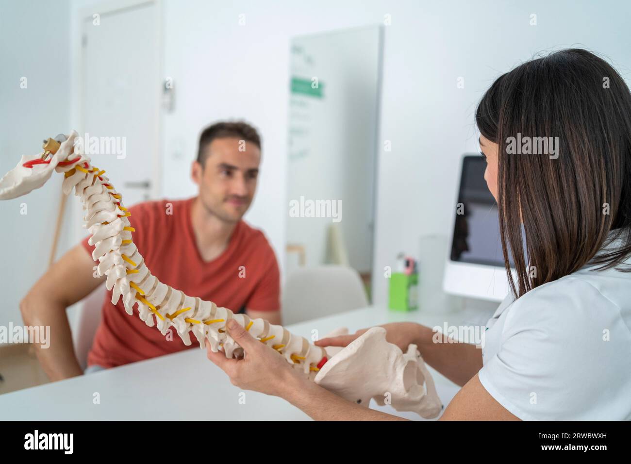 Professional female therapist in uniform showing spine to male patient while explaining problem of treatment during appointment in modern clinic Stock Photo