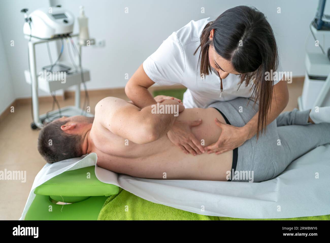 Calm young female therapist in white uniform rubbing back of male patient lying on table during massage treatment procedure in modern clinic Stock Photo