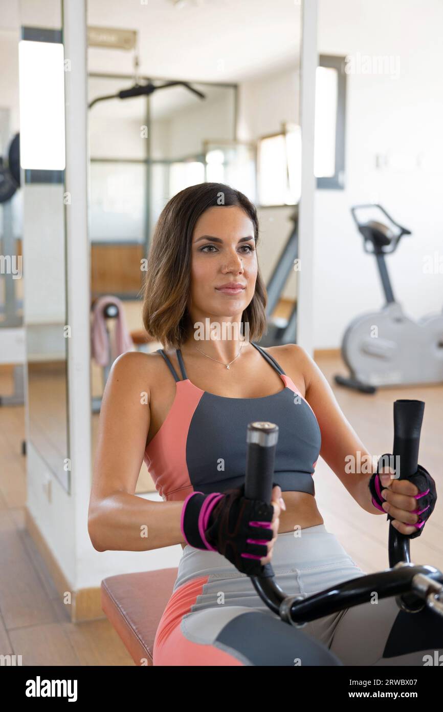 Serious strong adult woman doing seated cable row on equipment in gym looking away Stock Photo