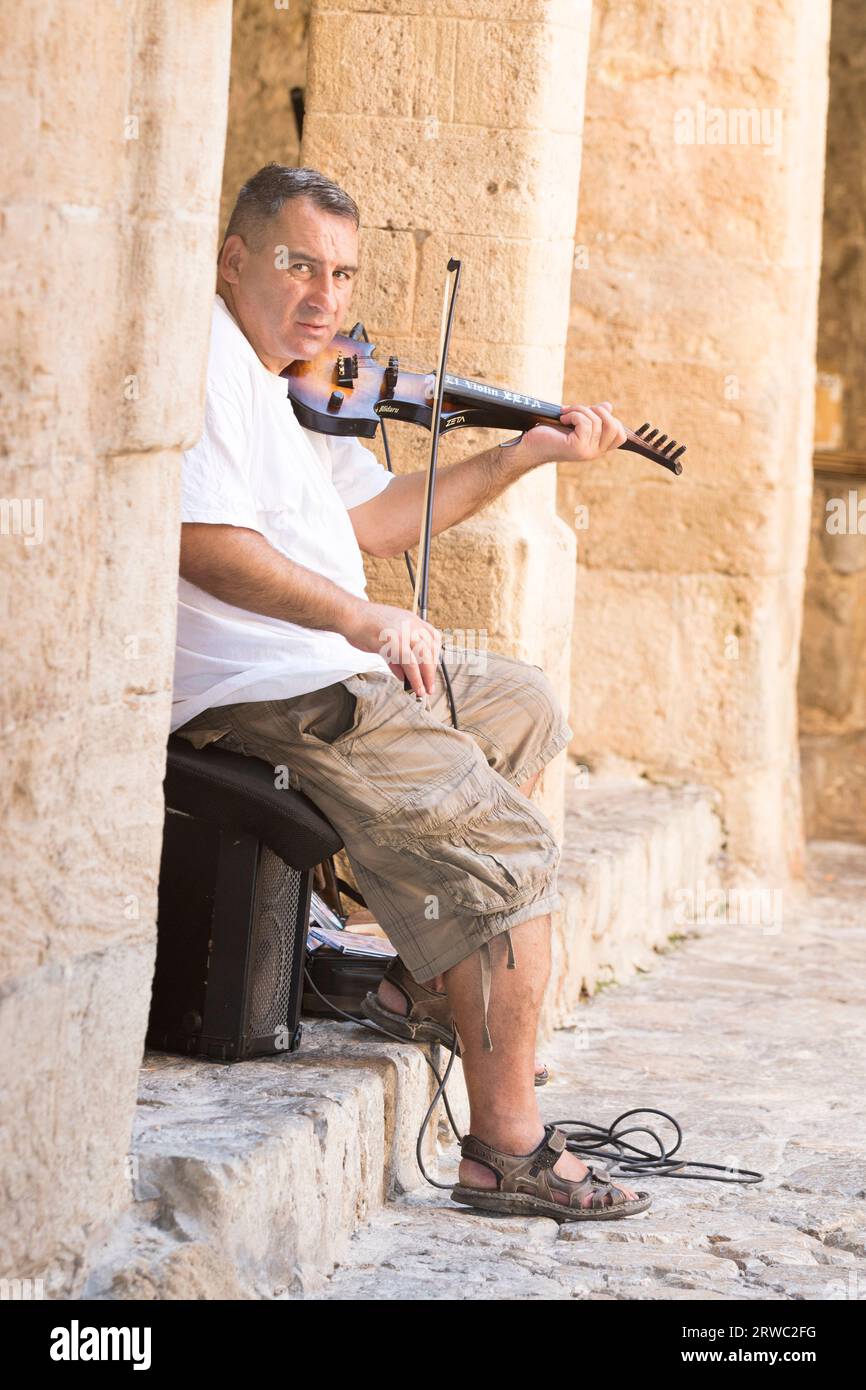 A male busker - eyes to camera - plays a violin in the side streets of Eivissa, Ibiza Old Town, Balearic Islands, Ibiza, Spain Stock Photo