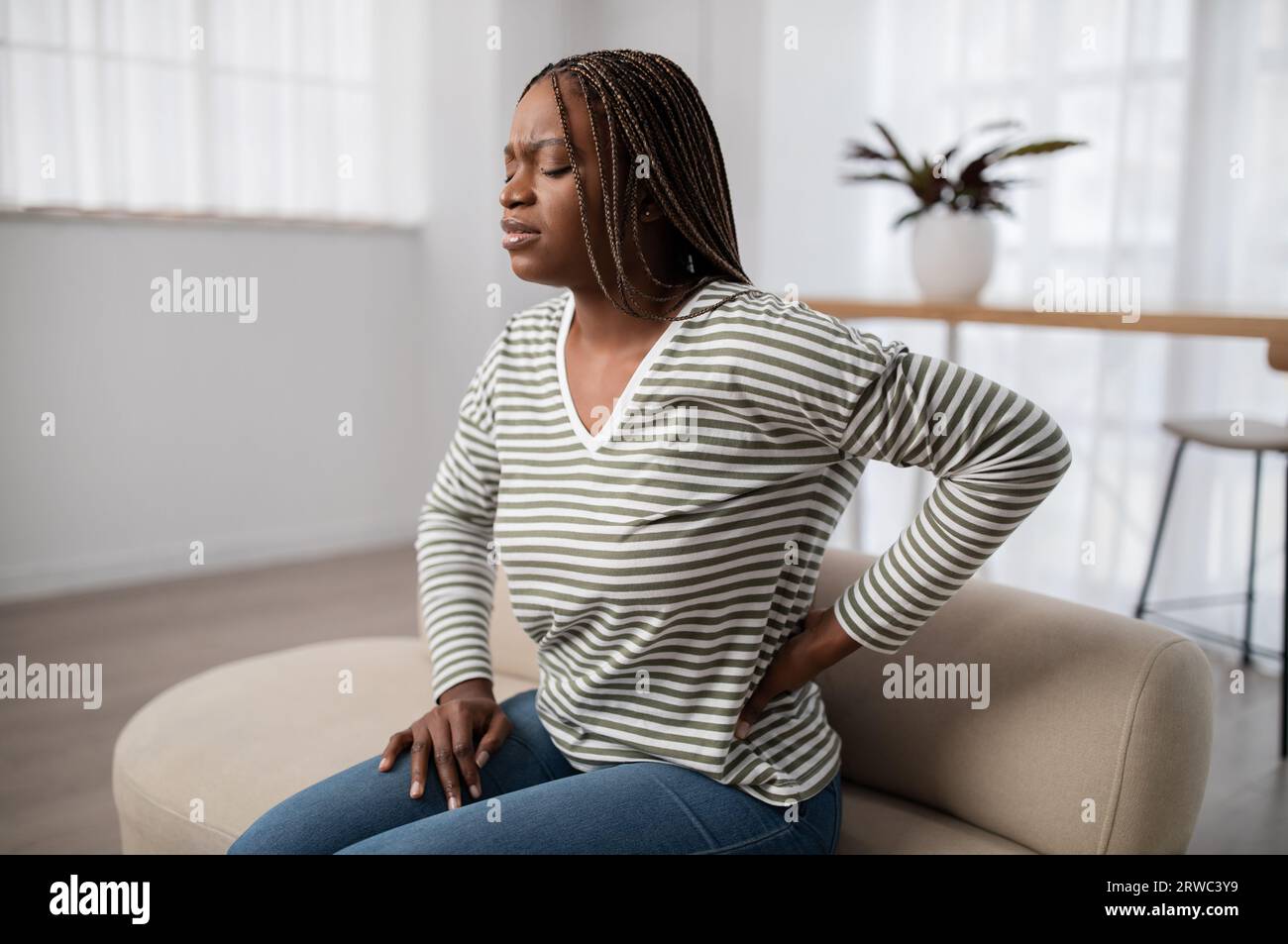 Unhappy Black Woman Sitting On Couch, Touching Back, Have Pain Stock 