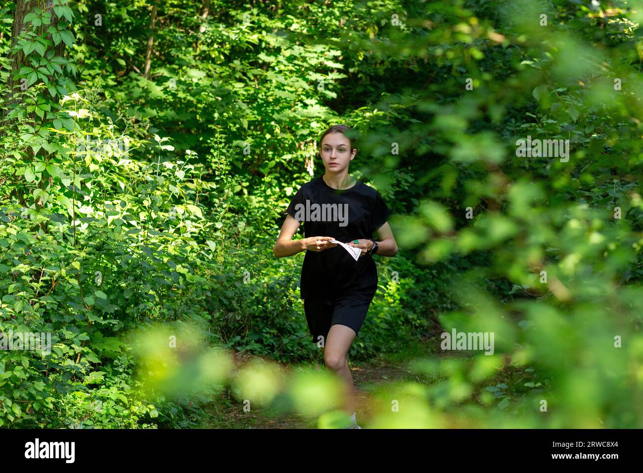 Young girl in forest reading map and searching for a control point. Sports orienteering competition. Athlete teenager girl moving to the control point Stock Photo