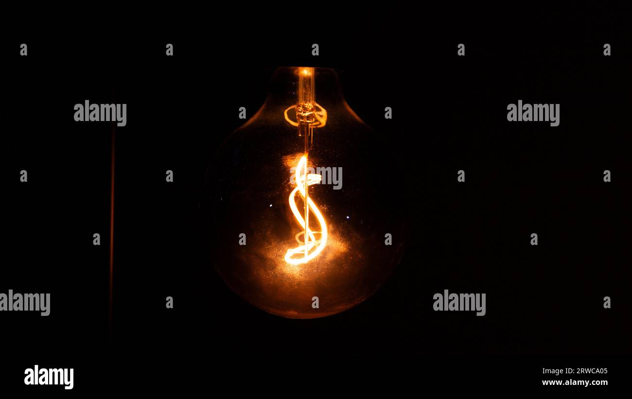 Glowing orange lightbulb in dark room Stock Photo