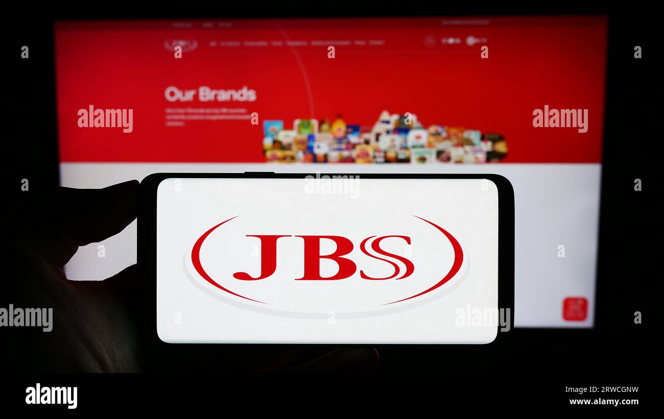 Person holding smartphone with logo of Brazilian mear processing company JBS S.A. on screen in front of website. Focus on phone display. Stock Photo