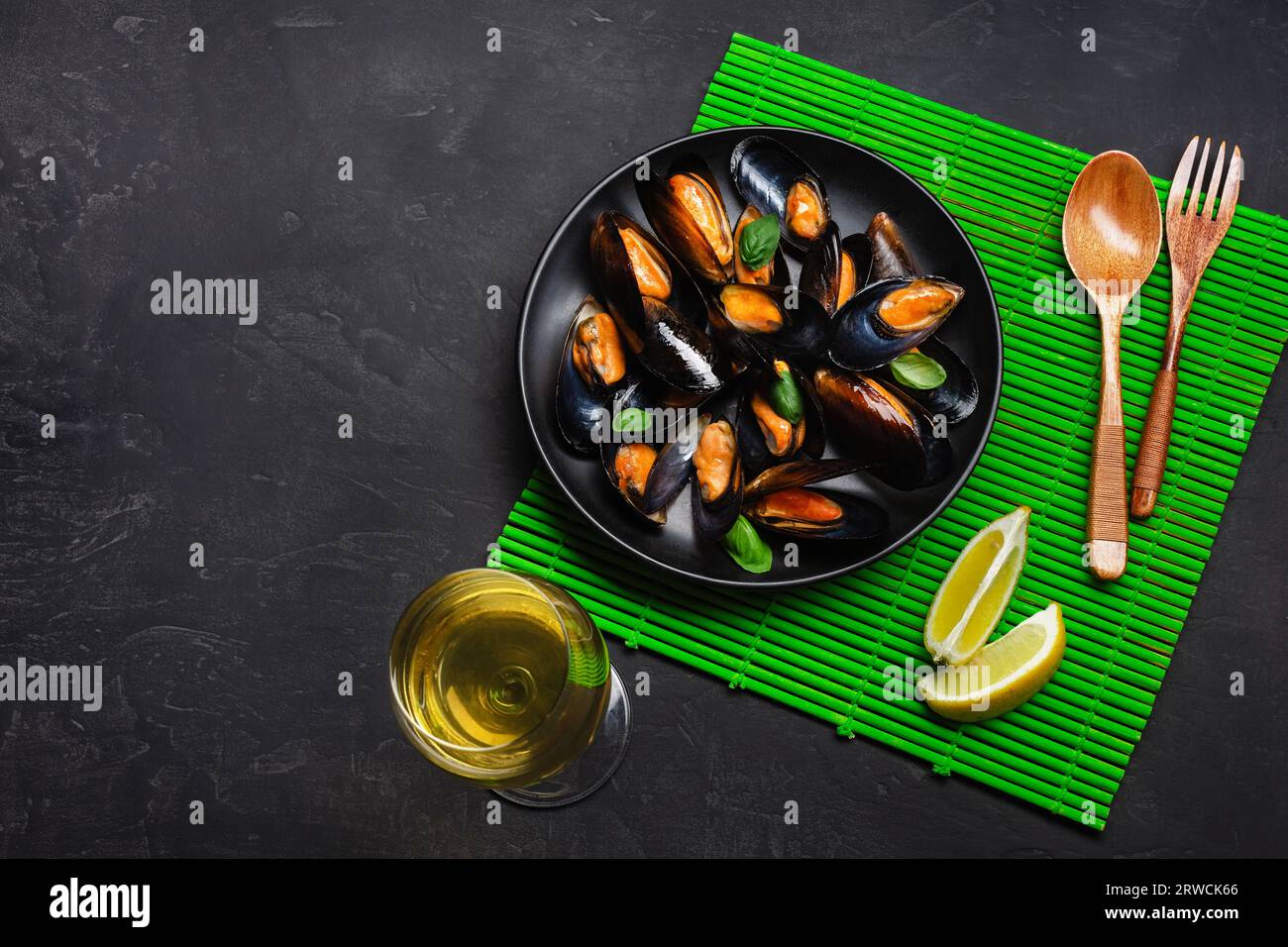 Seafood mussels, basil leaves in a black plate with wineglass, lemon