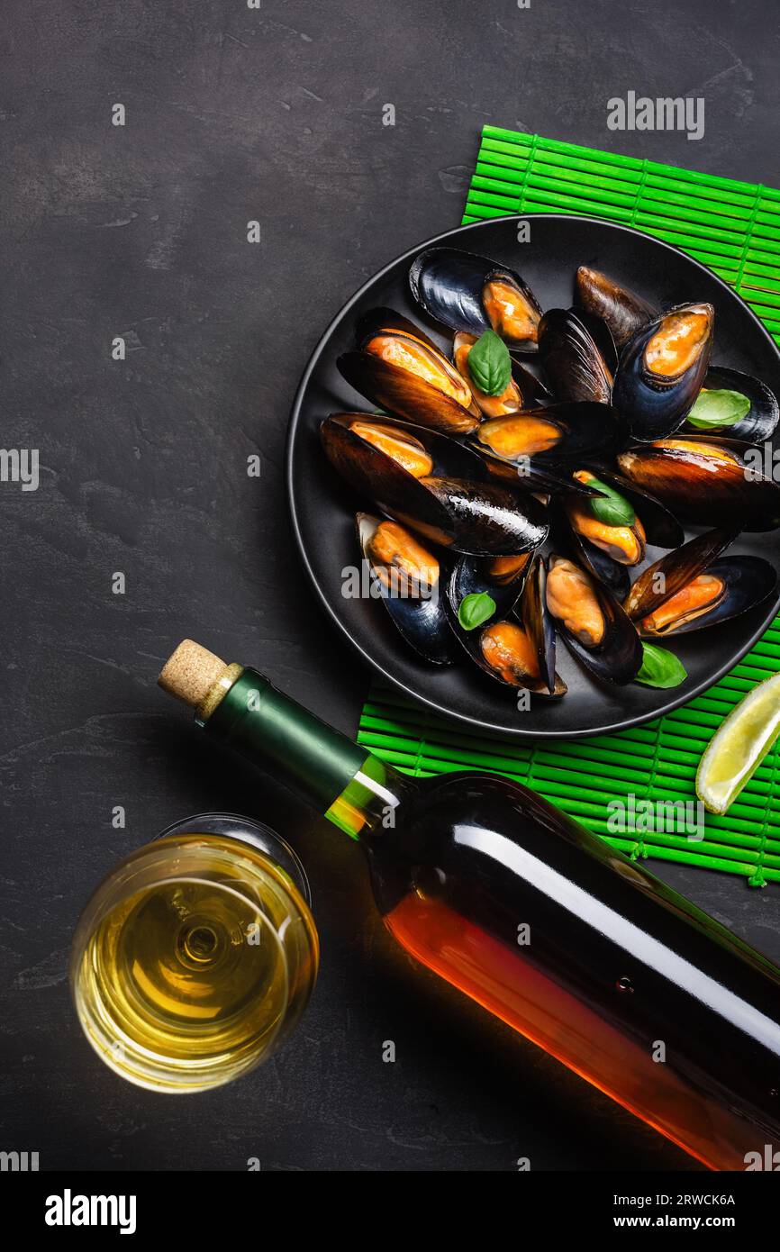 Seafood mussels, basil leaves in a black plate with wine bootle