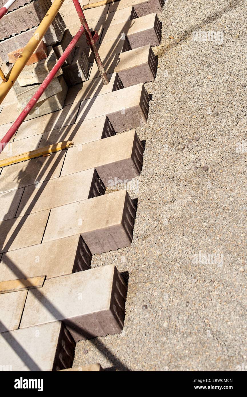 Half-placed cement blocks to create the asphalt of a pedestrian street with fences protecting the work and stacked bricks ready to be placed. Stock Photo