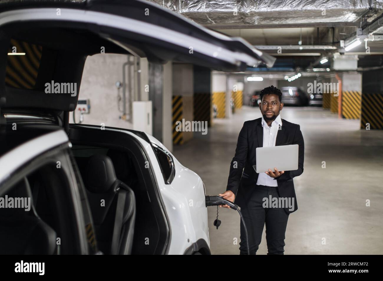 Man with computer plugging in EV charging cord in parking Stock Photo