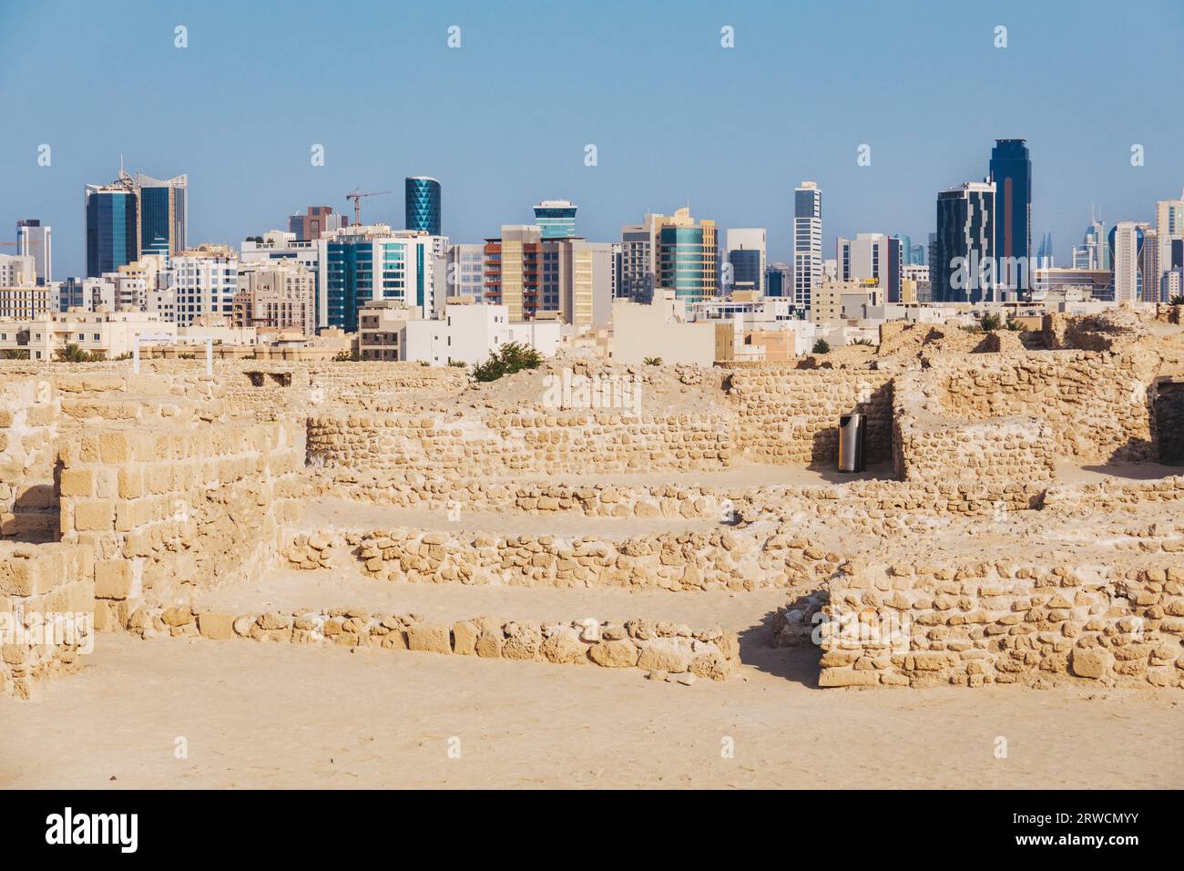 Old and new: the ruins of Bahrain Fort, dating back to 2300 BCE, against the modern skyline of downtown Manama city Stock Photo