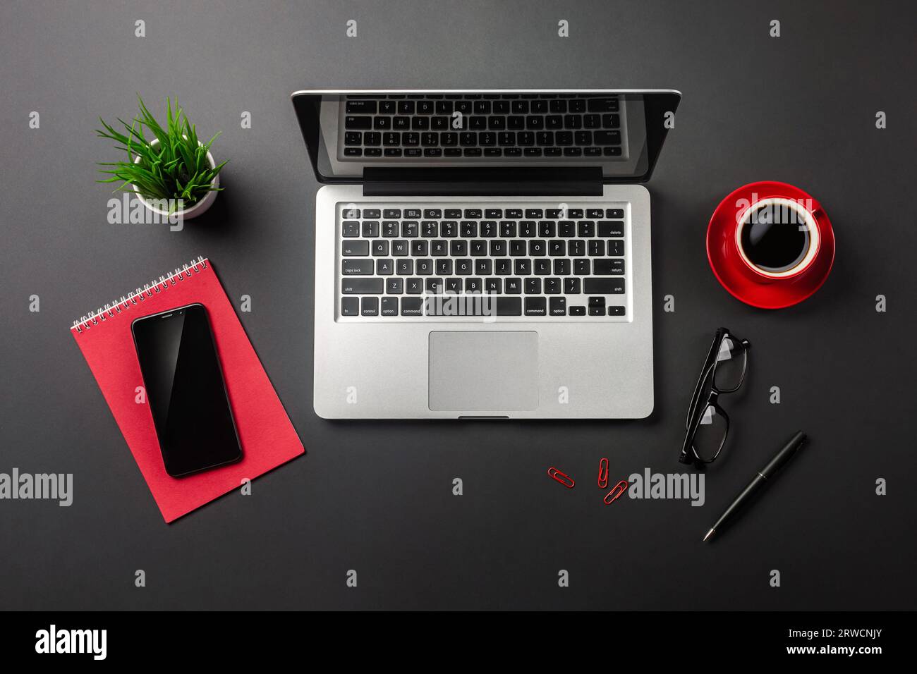 Black office desk table with blank screen laptop computer, notebook, mobile phone and red cup of coffee. Top view. Stock Photo