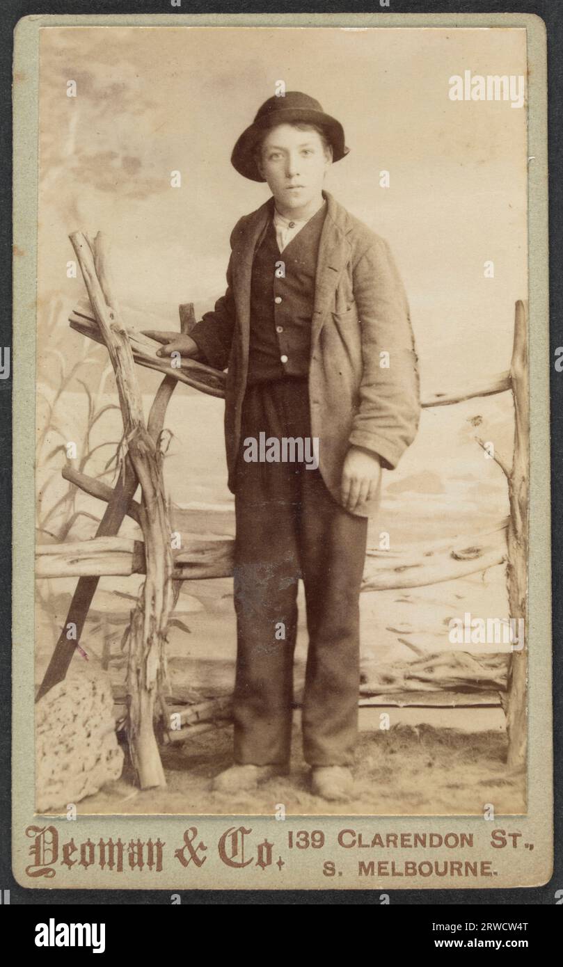 Edward Quinton. Studio portrait of a boy, full face, full length, standing with right hand resting on wooden fence. 1894. Stock Photo