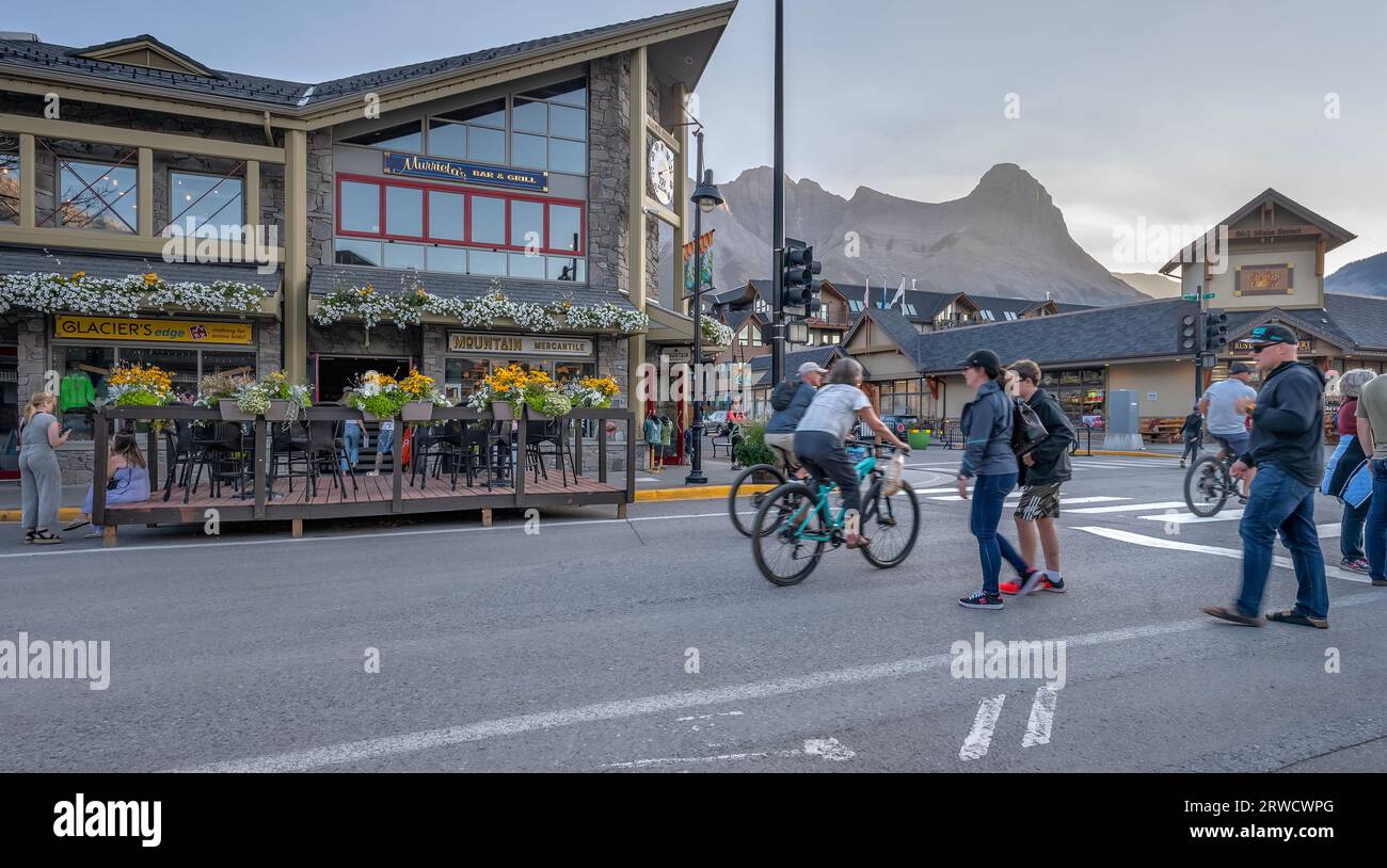 Canmore, Alberta, Canada – September 16, 2023:  People walk and ride bicycles on Main Street in the evening light Stock Photo