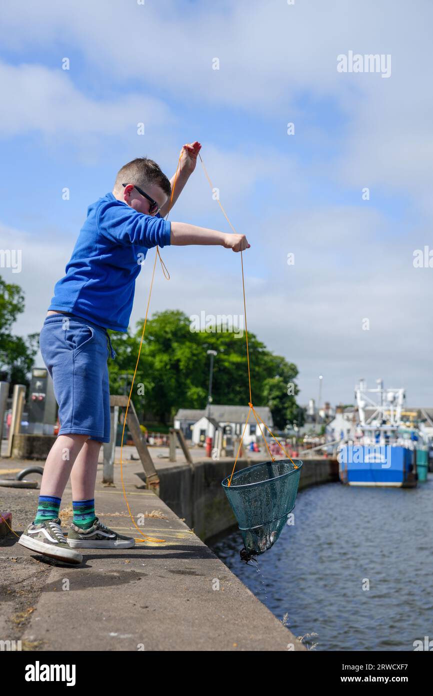 Young boy fishing for crabs off Kirkudbright harbour Stock Photo