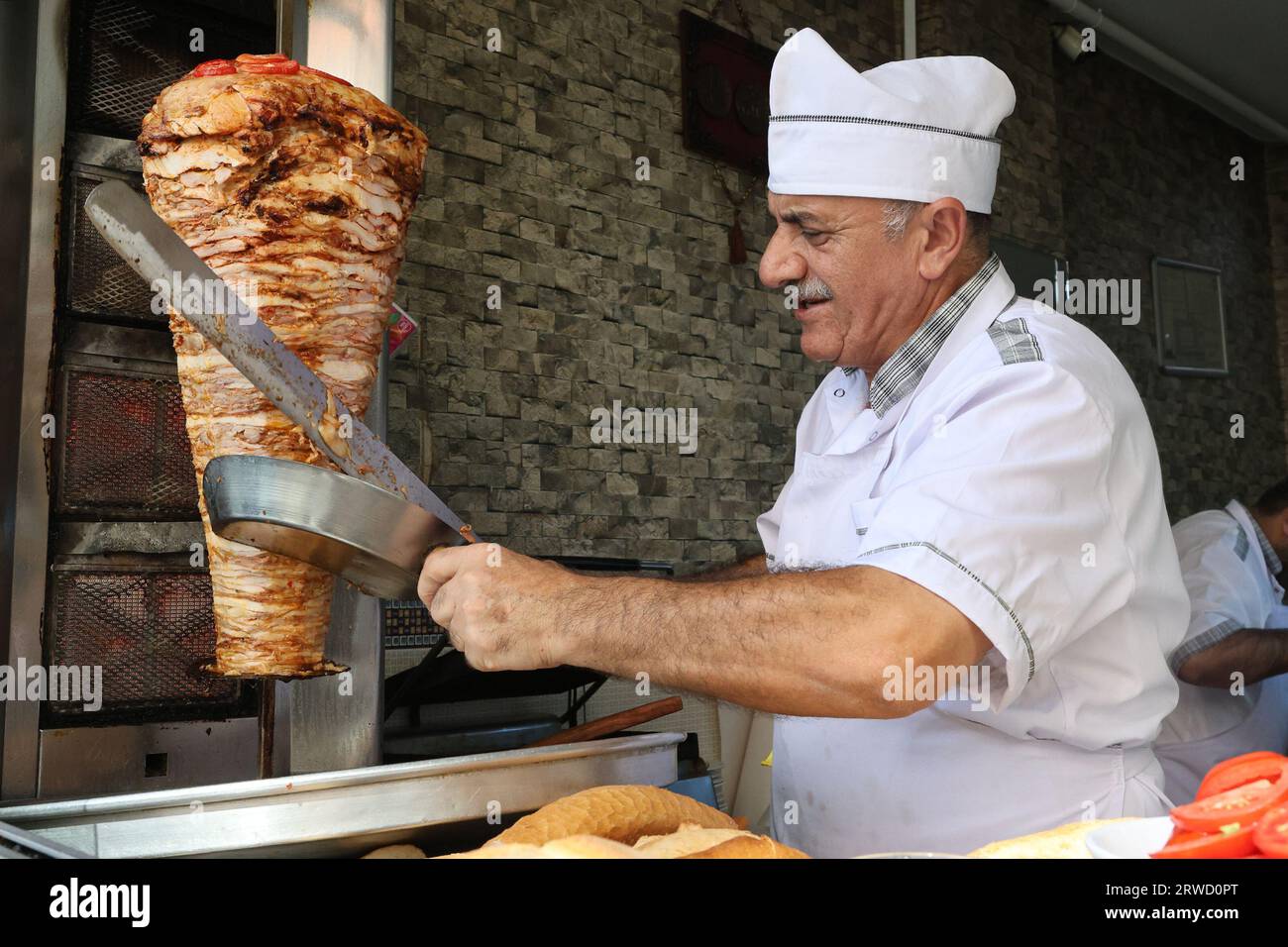 A chef slices meat with a knife to prepare a doner kebab at a restaurant in Istanbul Stock Photo
