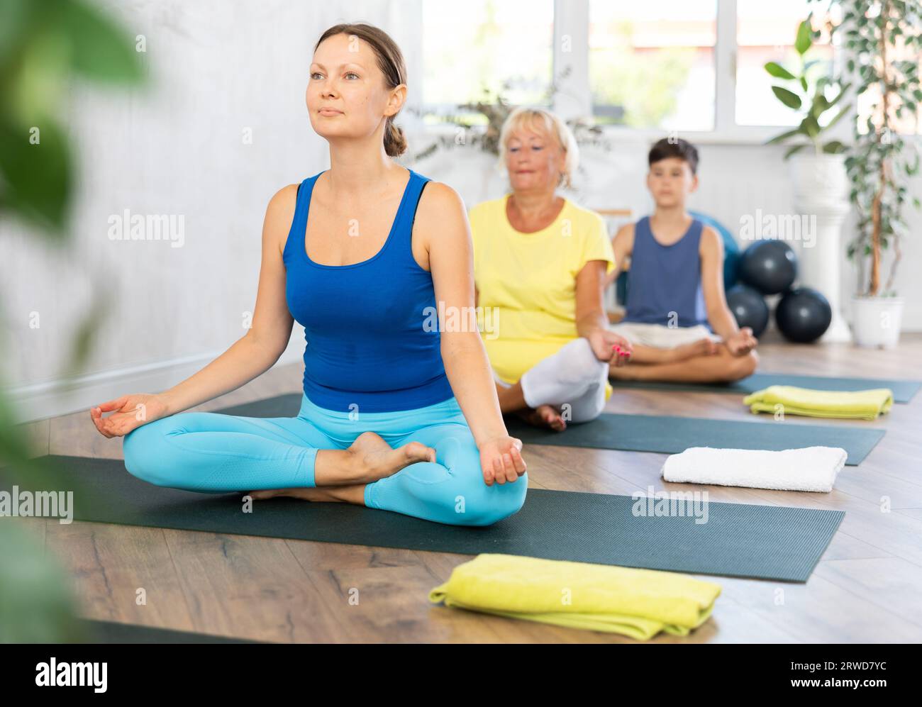 Middle-aged woman practicing half lotus pose of yoga in light fitness ...